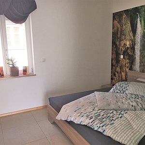 Schlafzimmer mit Doppelbett vor Wanddekoration mit schöner Fototapete die einen Wasserfall in der Natur zeigt